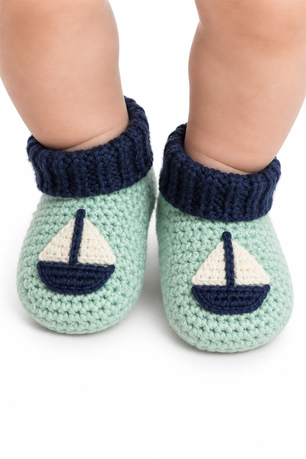 Mint crochet baby booties decorated with a small sailboat motif